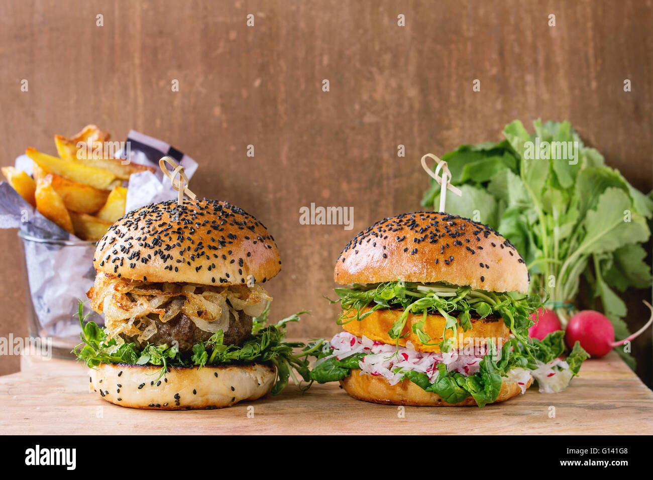 Hausgemachte traditionelle und Veggie Burger mit Rindfleisch, gebratenen Zwiebeln, süße Kartoffeln, Radieschen und Erbsen-Sprossen, diente über Holz Textur Stockfoto