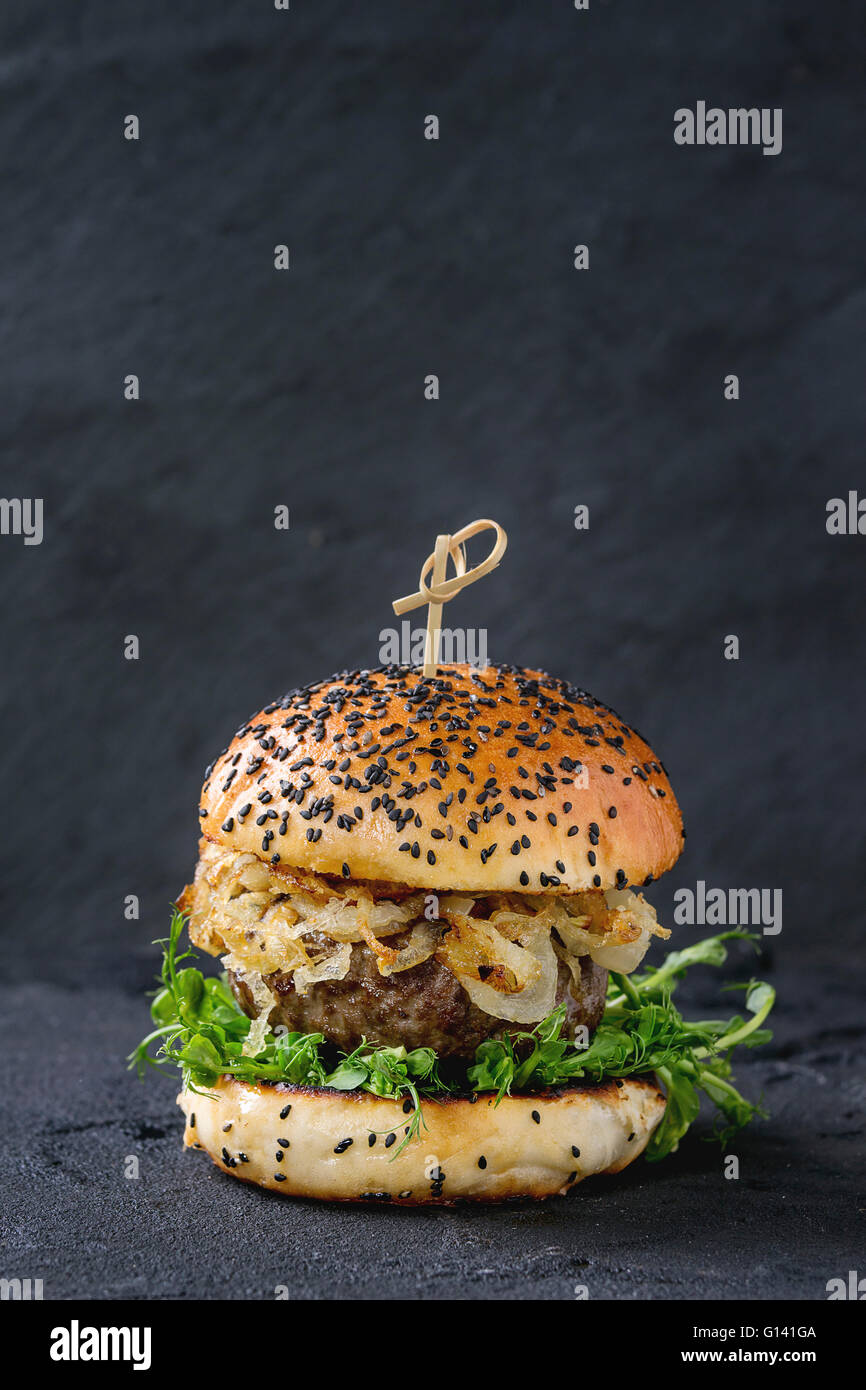Hausgemachte Burger mit Rindfleisch, gebratenen Zwiebeln und Erbsen-Sprossen, serviert auf schwarzem strukturierten Hintergrund Stockfoto