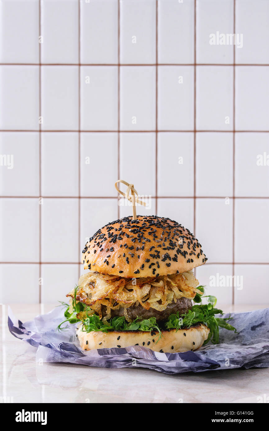 Hausgemachte Burger mit Rindfleisch, gebratenen Zwiebeln und Erbsen-Sprossen, serviert auf Packpapier über weißen Marmor Tisch mit Ziegel-Mauer bei bac Stockfoto