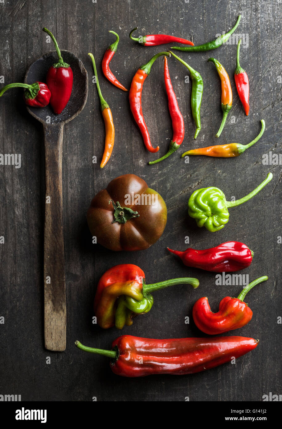 Rote und grüne Gemüse und rustikale alte Löffel auf dunklem Holz, Ansicht von oben. Paprika, Chilis und Kumato-Tomaten Stockfoto