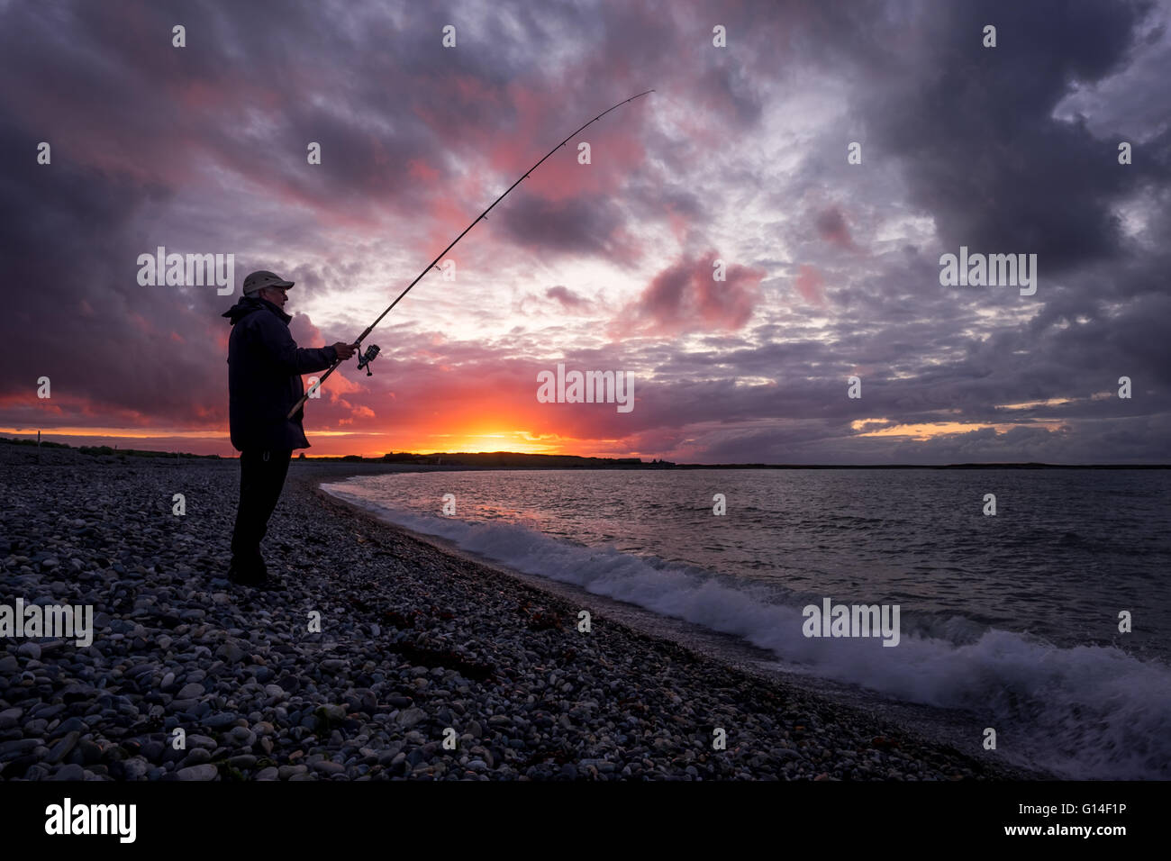 Ein Mann angeln im Meer am Strand bei Sonnenuntergang in Anglesey Stockfoto