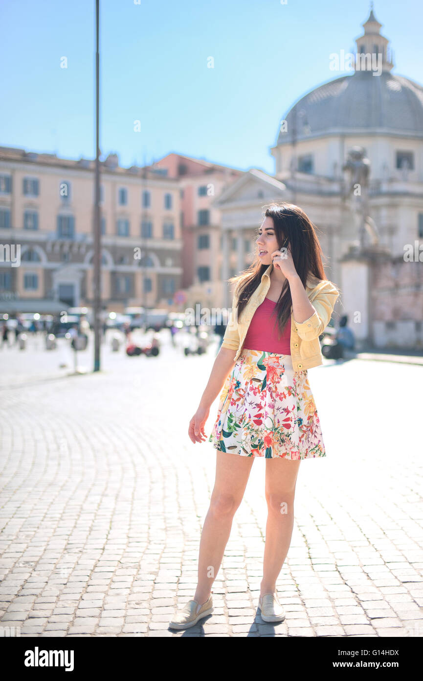 Junge Frau im Gespräch am Mobiltelefon auf der Piazza del Popolo mit Kirchenkuppel im Hintergrund Stockfoto