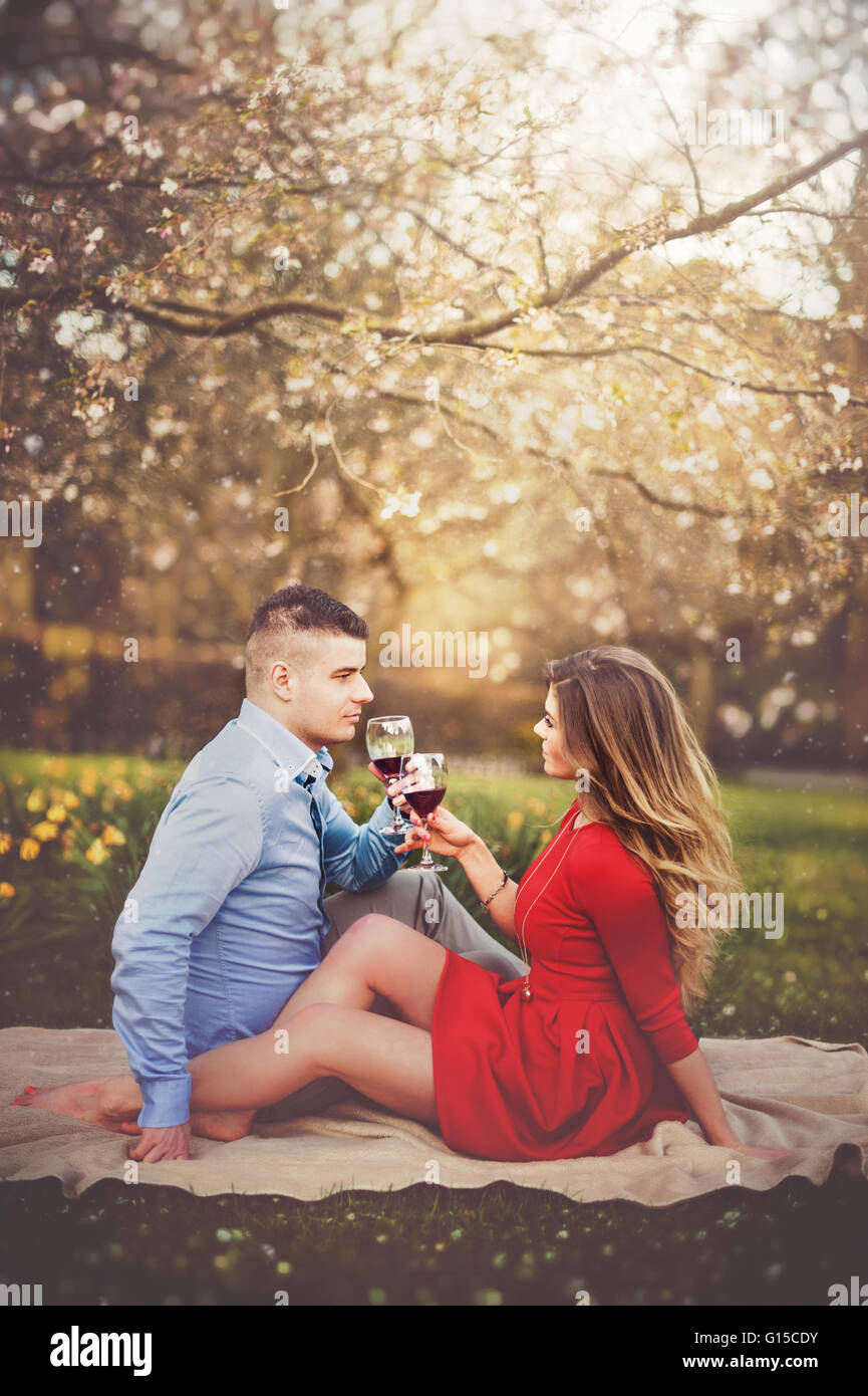 junges Paar Feier mit Glas Rotwein in der Natur unter dem blühenden Baum Stockfoto