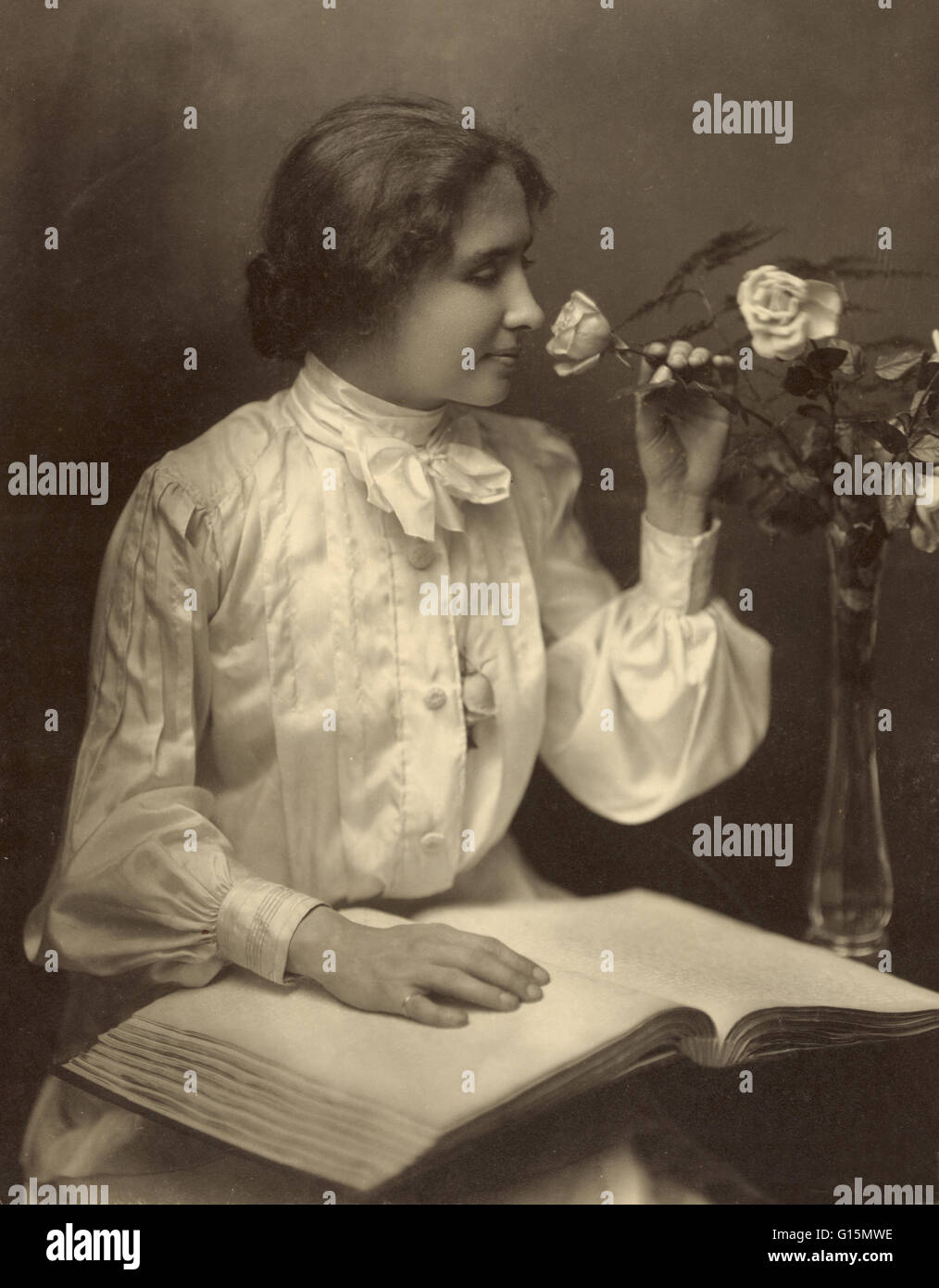 Helen Keller, 28. Oktober 1904. Foto zeigt, dass Keller mit Hand auf Braille-Buch auf dem Schoß sitzen, wie sie eine Rose in einer Vase riecht. Helen Adams Keller (27. Juni 1880 - 1. Juni 1968) war ein US-amerikanischer Autor, politischer Aktivist und Dozent. Sie war 19 mo Stockfoto