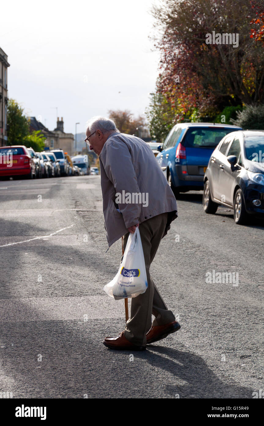 Älterer senior Mann beim Überqueren der Straße mit Einkaufstasche und Spazierstock Stockfoto