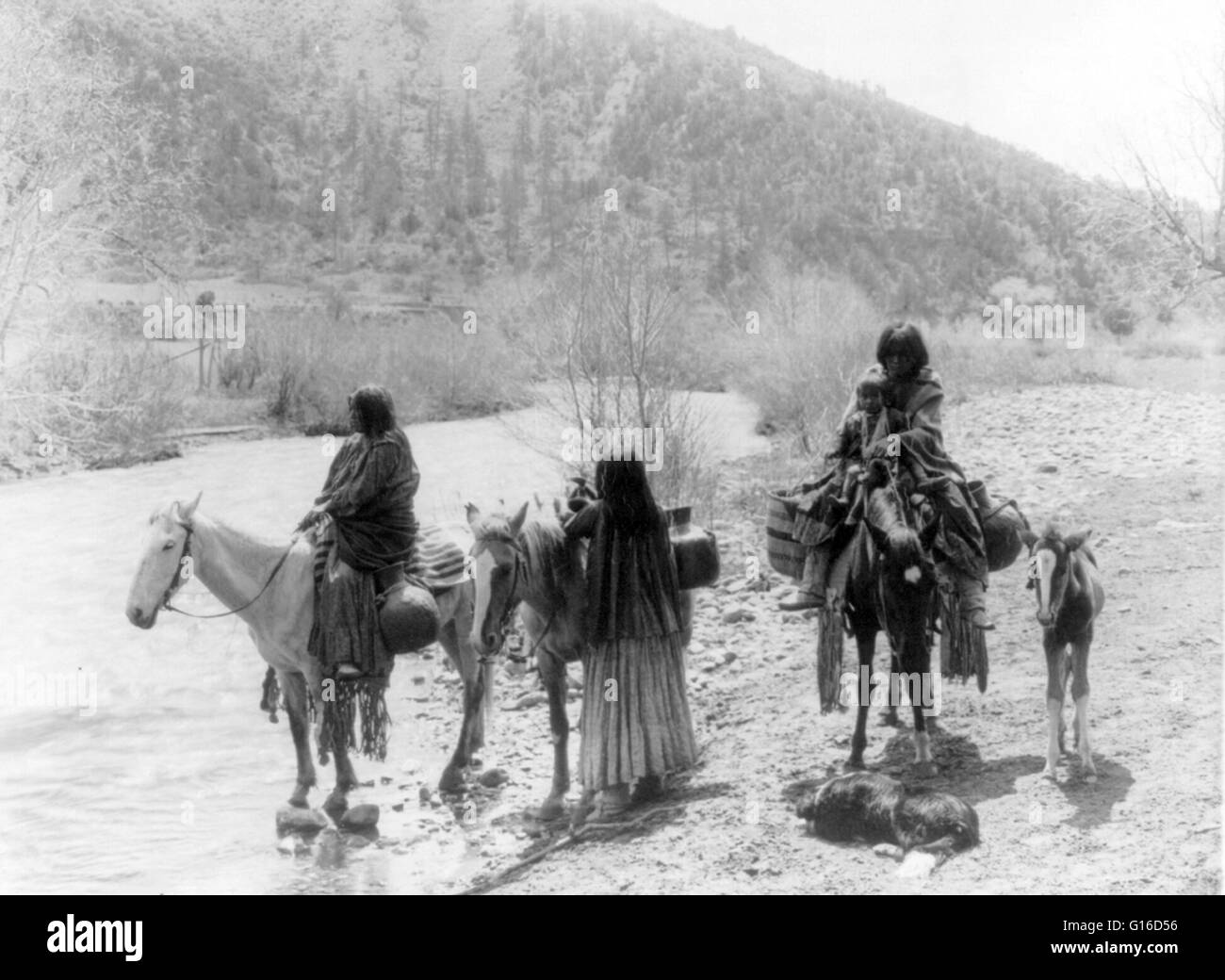 Titel: "an der Furt" fotografiert von Curtis, 20. Juli 1903. Drei Apachen, einer mit einem Kind mit Pferden beladen mit Wasser Krüge, ein Fohlen und ein Hund nicht mehr neben einem Bach. Apache ist der Sammelbegriff für verschiedene kulturell-bezogene Gruppe von Stockfoto