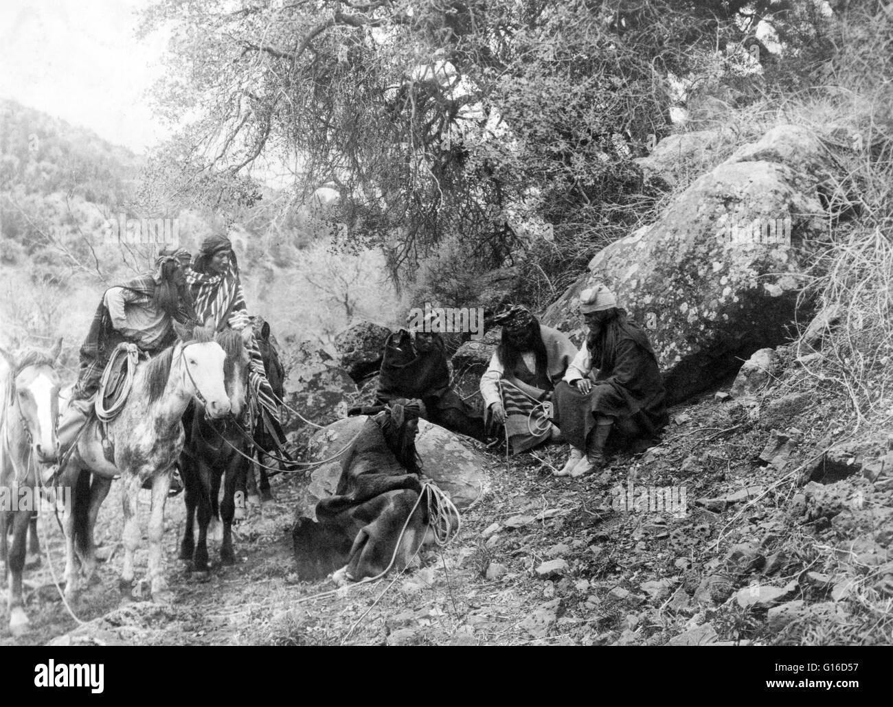 Unter dem Titel: "Storytelling" fotografiert von Curtis, 1906. Gruppe von Apache Männer, zwei auf dem Rücken der Pferde, andere sitzen, hören und schauen auf als ein Mitglied der Partei ist die Kennzeichnung des Boden mit einem Stock. Apache ist der Sammelbegriff für mehrere cultur Stockfoto