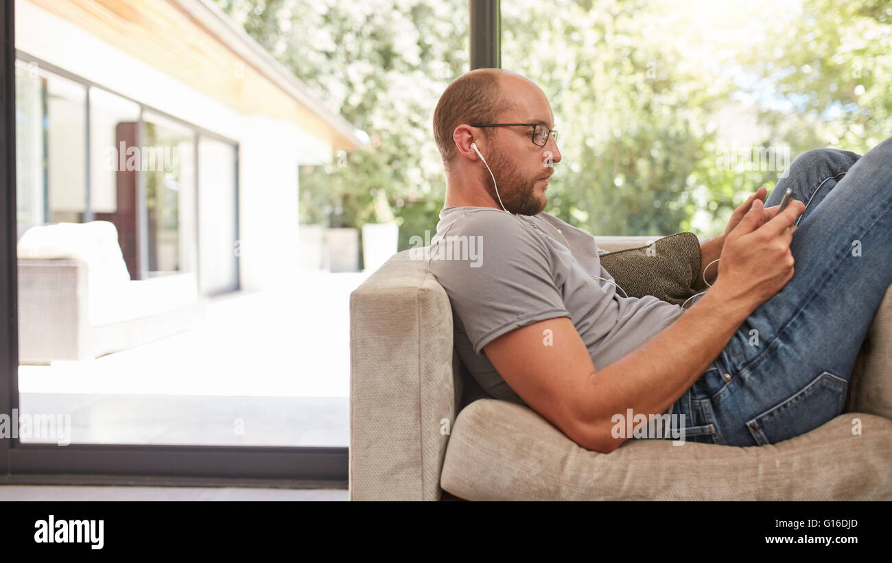 Side-View-Bild eines Mannes mit seinem Tablet beim Sitzen auf dem Sofa zu Hause. Entspannen Sie sich auf die Couch mit kaukasischen Mann tablet-pc. Stockfoto