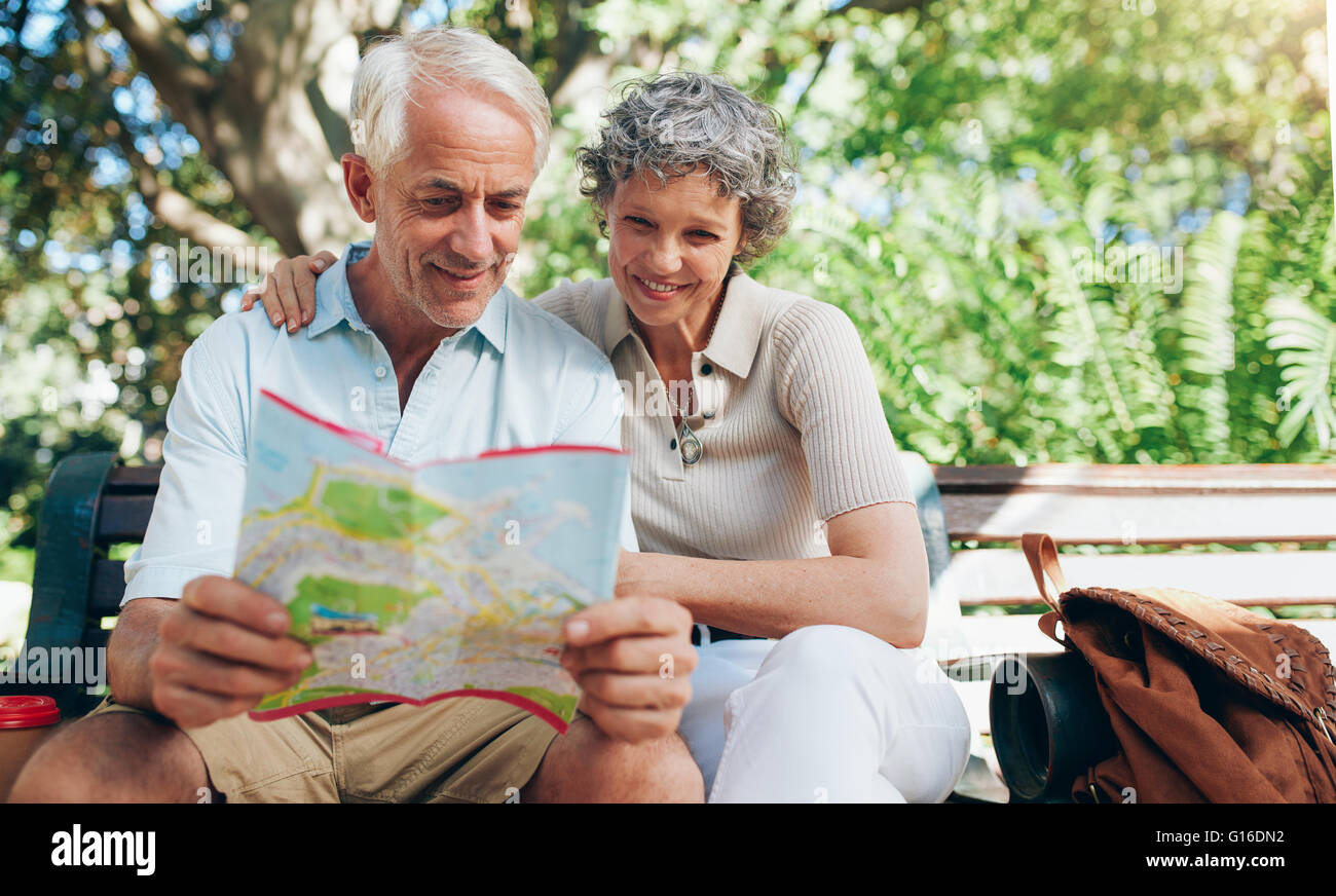 Gerne älteres Paar mit Stadtplan für Richtung. Ehepaar im Ruhestand auf einen Urlaub im Freien auf einer Parkbank sitzen und lesen einen ma Stockfoto