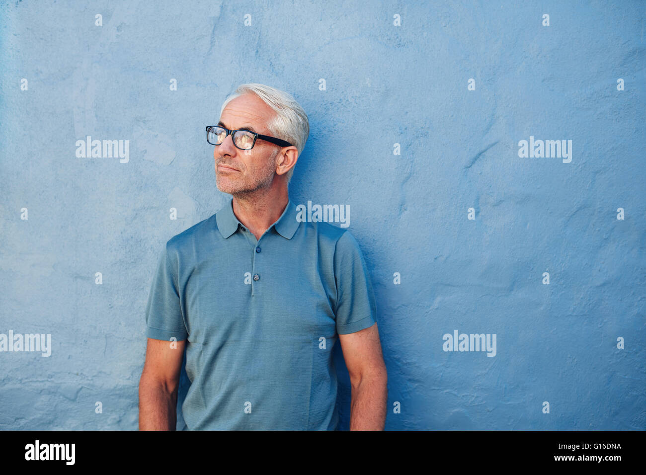 Porträt einer nachdenklichen reifer Mann steht vor einer blauen Wand und wegsehen. Kaukasischen Mitte erwachsener Mann mit Brille. Stockfoto