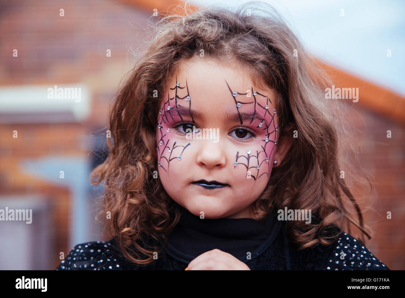 Kleines Mädchen mit Spinnennetz gemalt auf Gesicht, Blick in die Kamera. Halloween Stockfoto