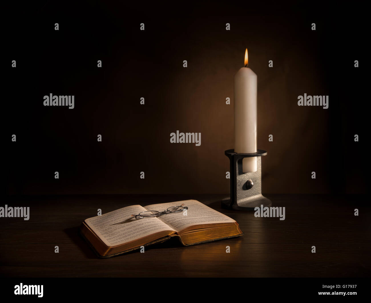 Altes Buch und Brille beleuchtet bei Kerzenschein in Eisen Kerzenständer Stockfoto