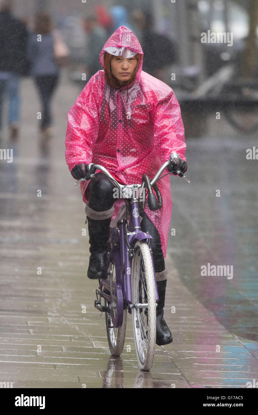 Eine asiatische Frau trägt einen rosa Poncho während der Fahrt ein Fahrrad bei nassem Wetter in Cardiff, Wales. Stockfoto