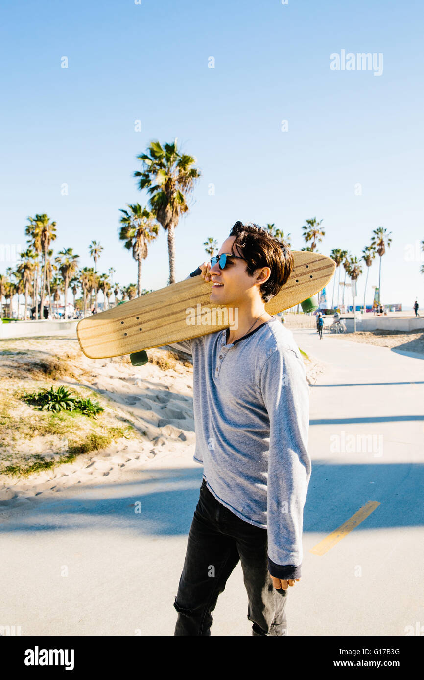 Junger Mann im freien laufen, Skateboard auf der Schulter tragen Stockfoto