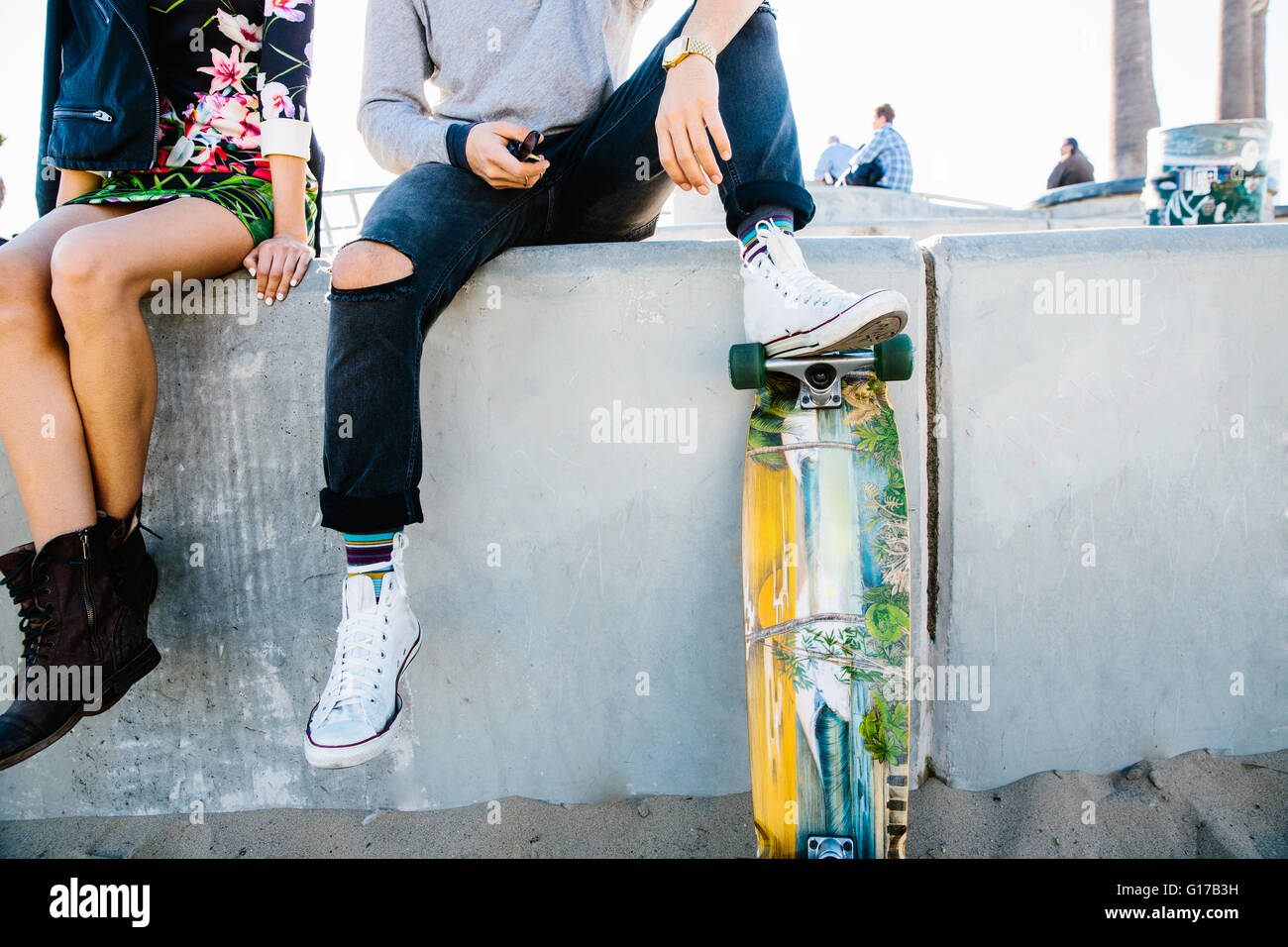 Junges Paar sitzt an Wand, Mann ruht Fuß auf Skateboard, niedrige Abschnitt Stockfoto