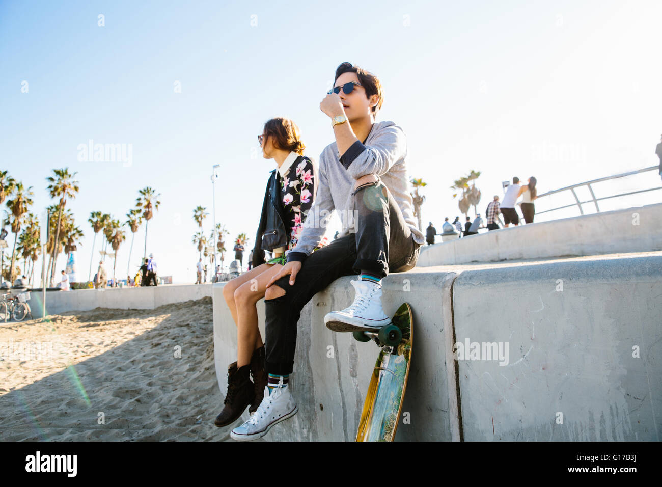 Junges Paar sitzt Mann ruht auf Wand, einen Fuß auf skateboard Stockfoto