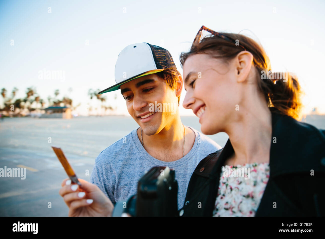 Junges Paar Blick auf sofortige Foto an Küste, Venice Beach, Kalifornien, USA Stockfoto