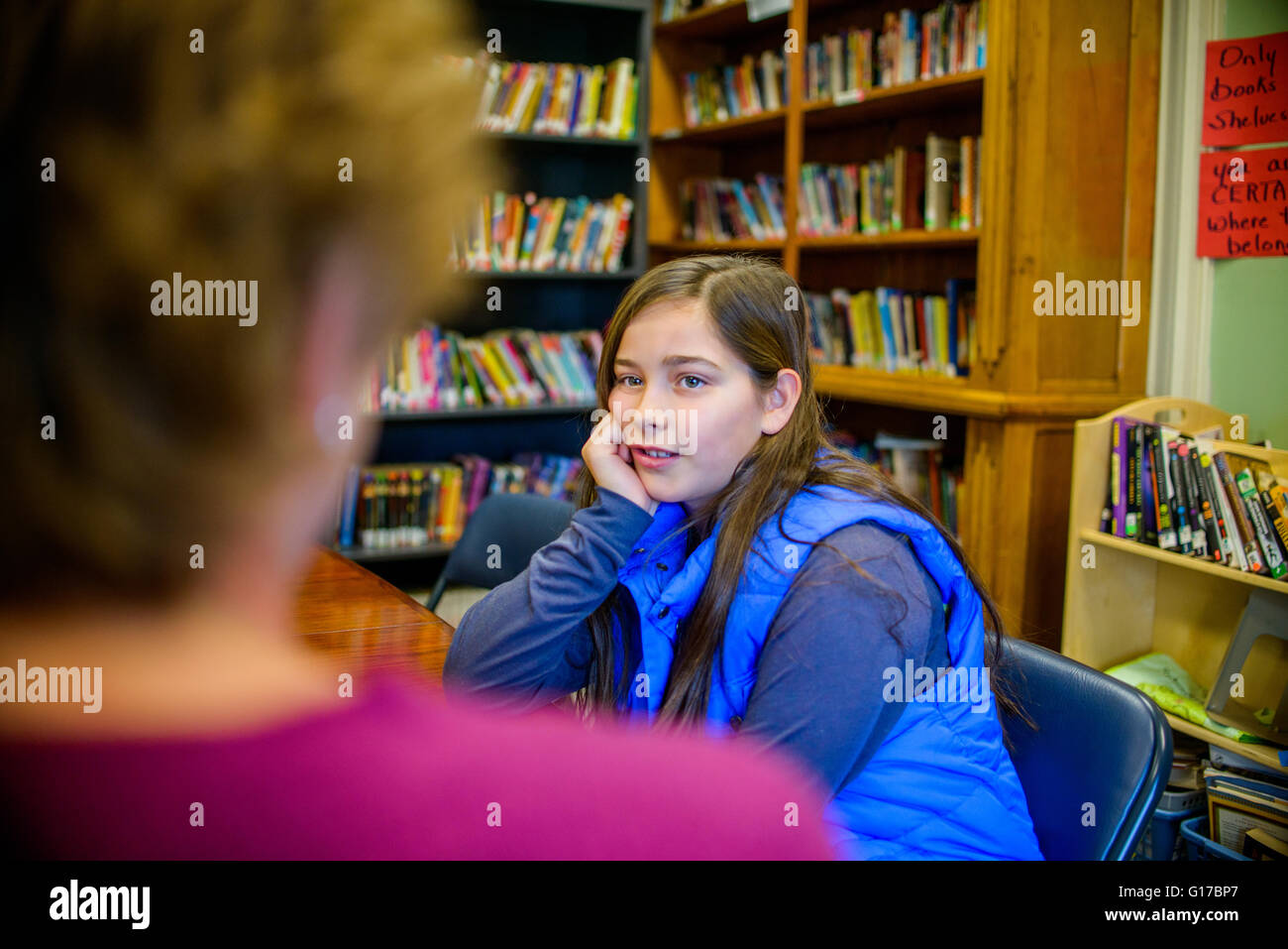 Teenager-Mädchen mit Hand am Kinn, in der Schulbibliothek im Gespräch mit dem Berufsberater Stockfoto