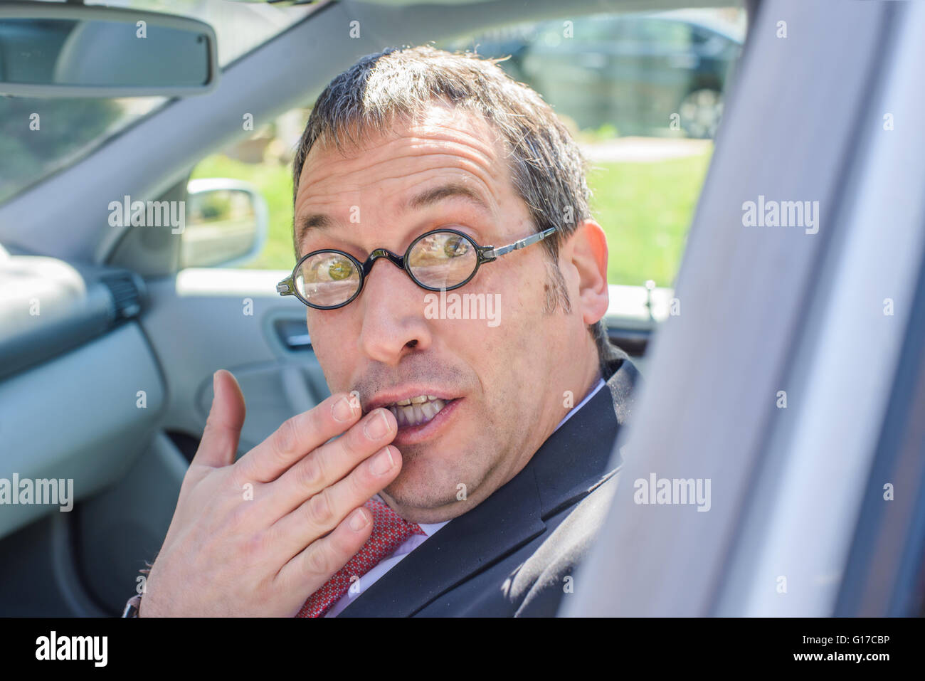 Mann im Auto tragen Brillen, Hand über Mund, Blick in die Kamera Stockfoto