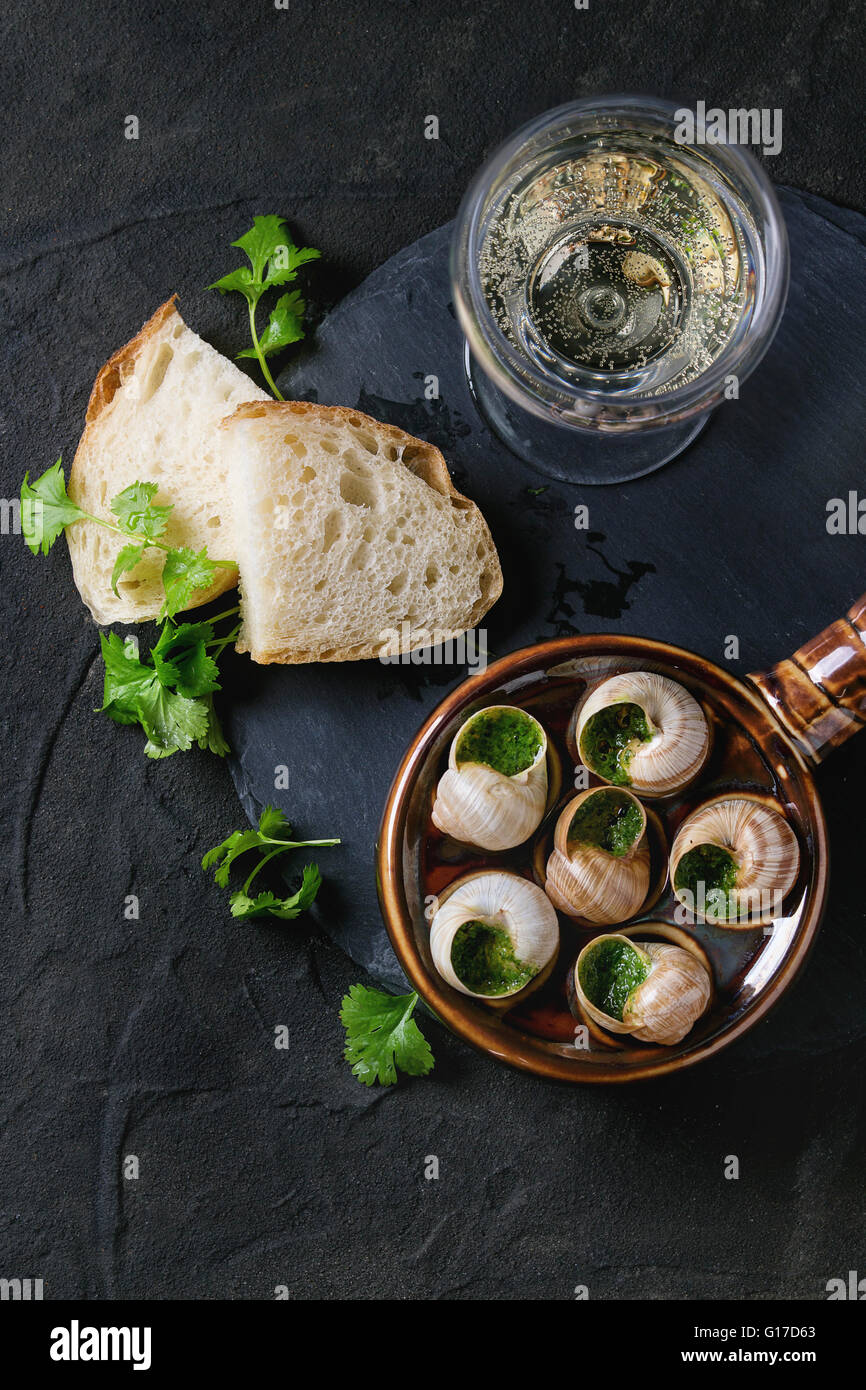 Escargots de Bourgogne - Schnecken mit Kräuter-butter, Gourmet-Gericht, in traditionellen keramischen Pfanne mit Petersilie, Brot und ein Glas whi Stockfoto