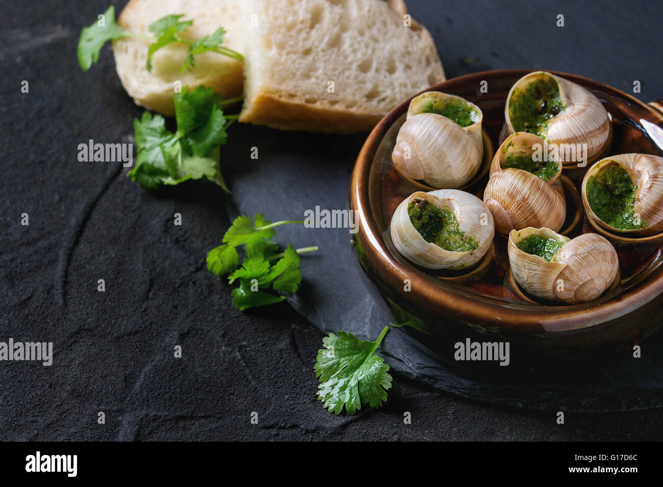 Escargots de Bourgogne - Schnecken mit Kräuter-butter, Gourmet-Gericht, in traditionellen keramischen Pfanne mit Petersilie und Brot auf Stein Lamelle Stockfoto