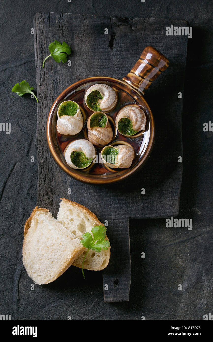 Escargots de Bourgogne - Schnecken mit Kräuter-Butter, in traditionellen Keramik Pfanne mit Petersilie und Brot auf hölzernen chopping Board o Stockfoto