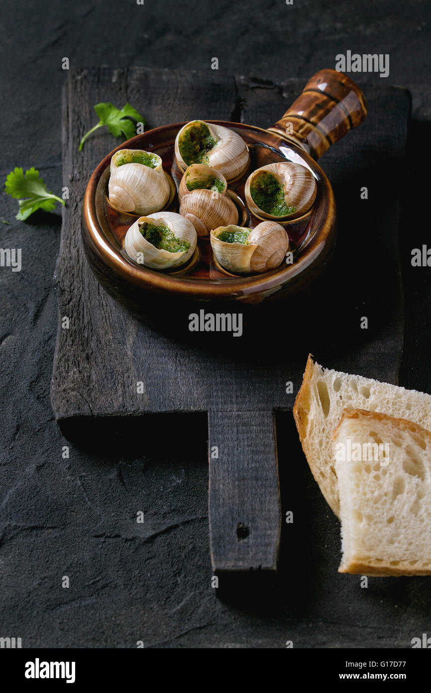 Escargots de Bourgogne - Schnecken mit Kräuter-butter, Gourmet-Gericht, in traditionellen keramischen Pfanne mit Petersilie und Toastbrot auf woo Stockfoto