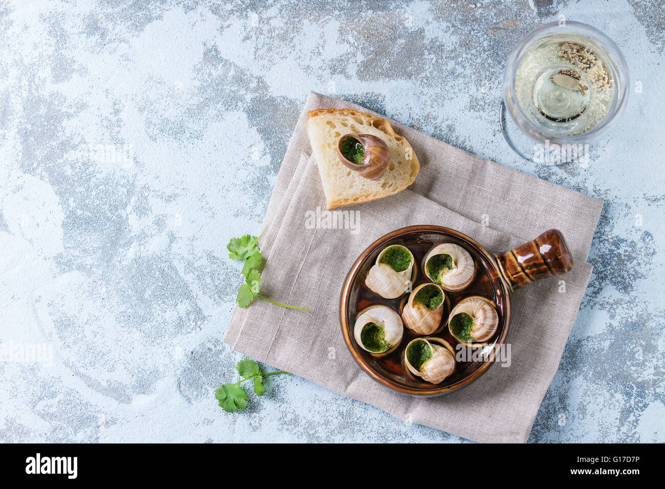 Escargots de Bourgogne - Schnecken mit Kräuter-Butter, in traditionellen keramischen Pfanne mit Petersilie, Brot und ein Glas Weißwein auf tex Stockfoto