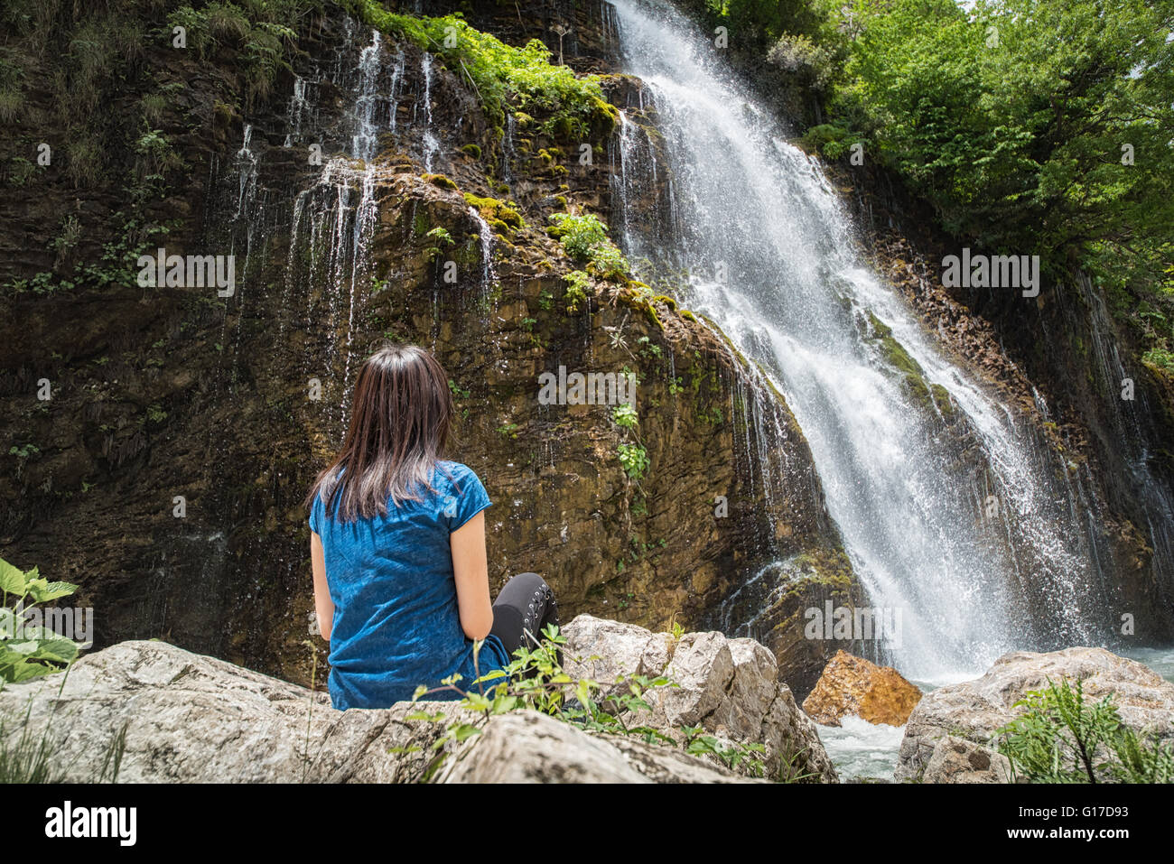 junge Frau sitzt und Blick auf den Wasserfall Stockfoto