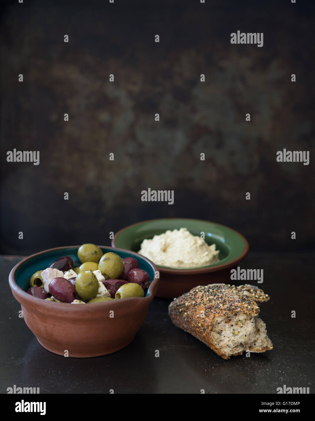 dunkle stimmungsvolle Stillleben Studioaufnahme von kleinen Schüsseln mit gemischten Oliven und Feta-Käse, Hummus und knusprigem Brot Stockfoto