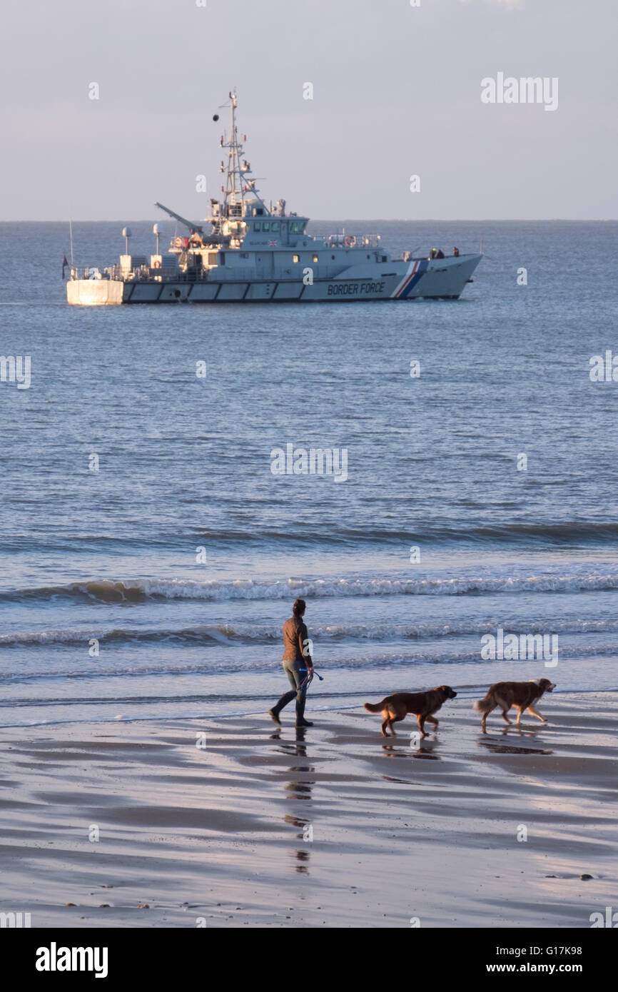 Eine Frau, die ihre Hunde Blick auf eine britische Grenze Force Schiff in Sandown Bay, Isle Of Wight Stockfoto