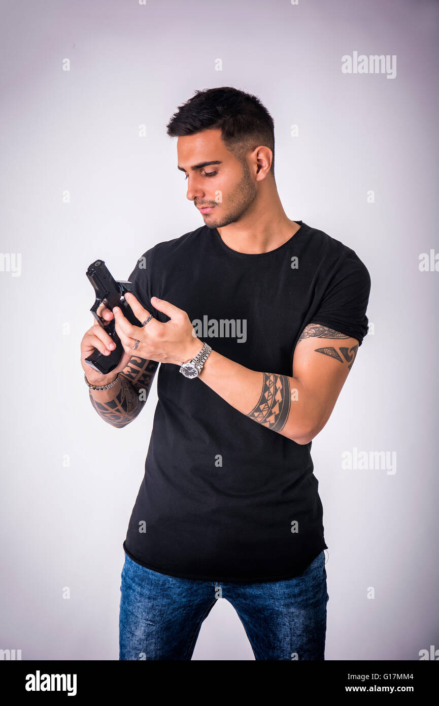 Schönen jungen Mann mit einer Handpistole tragen schwarzes T-shirt, auf hellem Hintergrund im studio Stockfoto