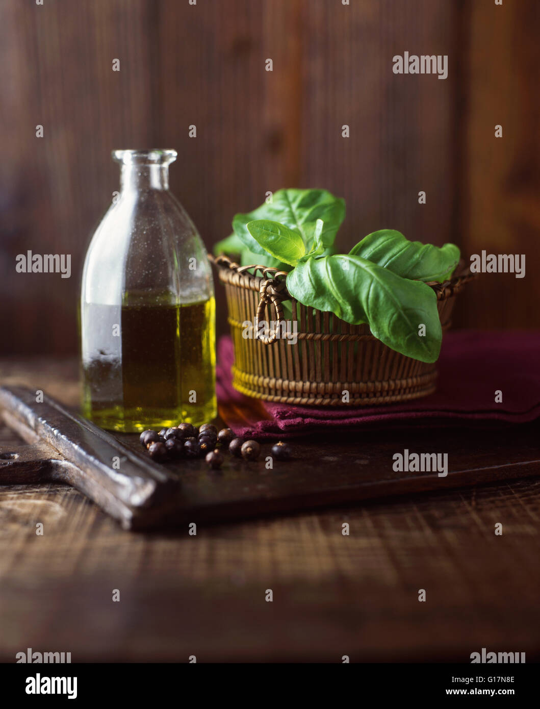 Extra natives Olivenöl, Basilikum und Wacholder Beeren auf Schneidbrett aus Holz Stockfoto