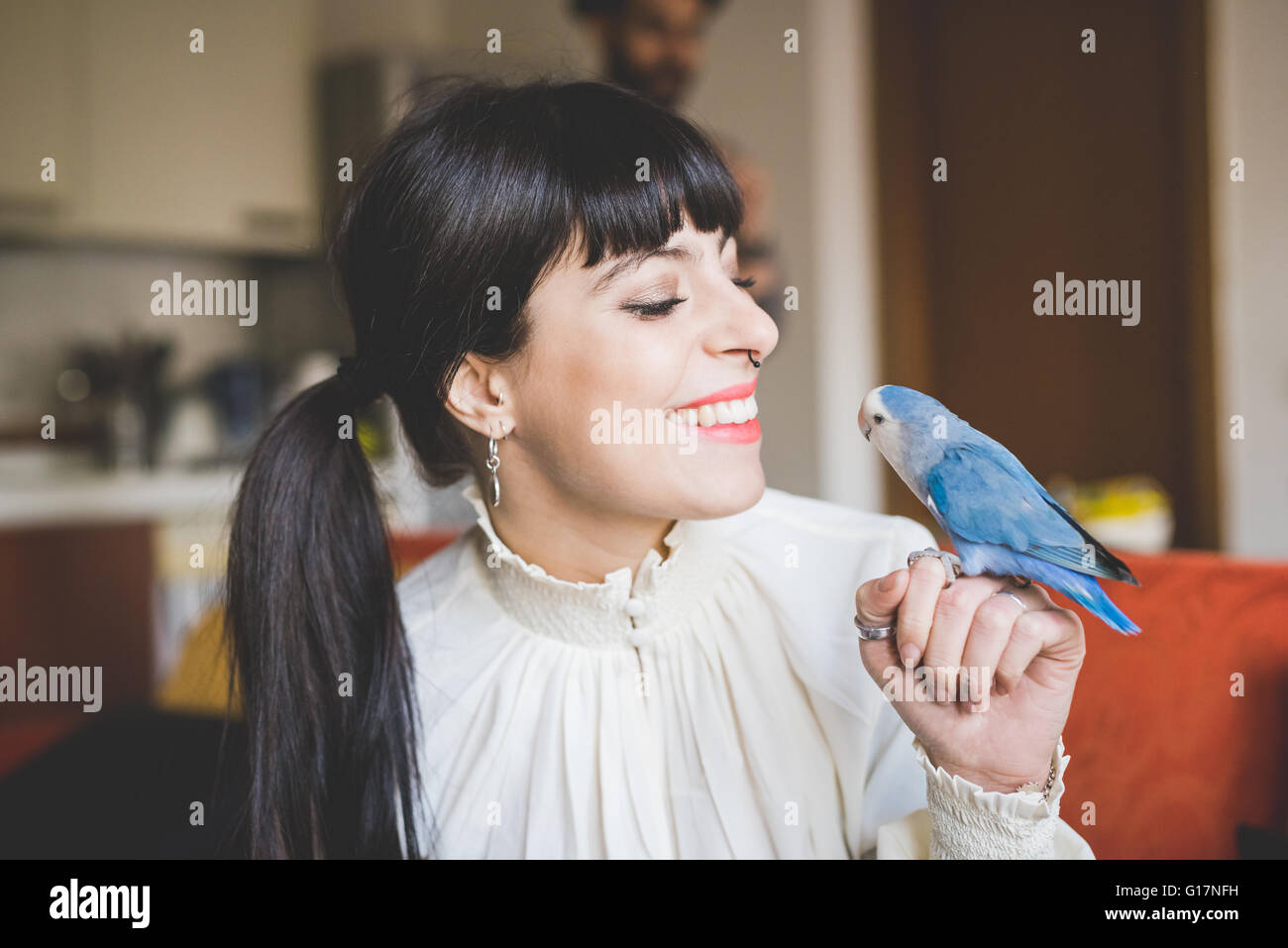 Junge Frau lächelte Haustier Vogel im Innenbereich Stockfoto