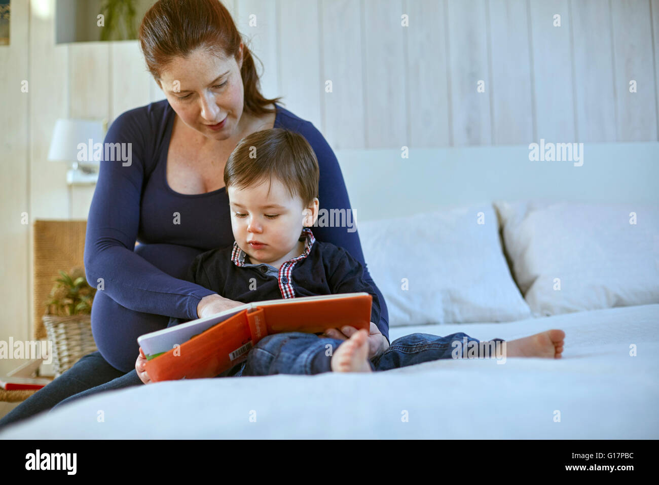 Schwangere Mutter und Baby Boy sitzt auf Bett Buch zusammen Stockfoto