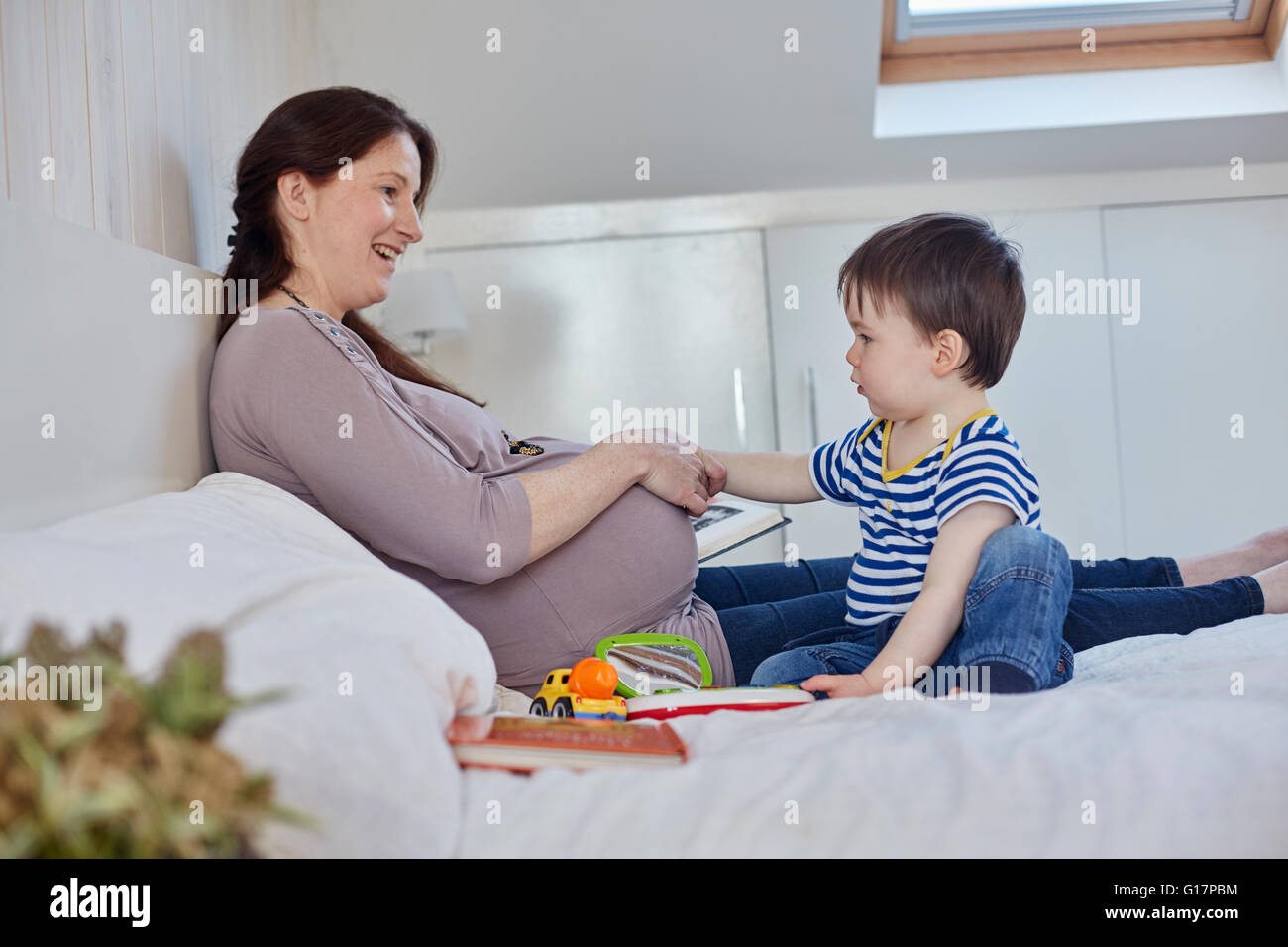 Seitenansicht des kleinen Jungen auf Bett Mütter schwanger Bauch zu berühren Stockfoto