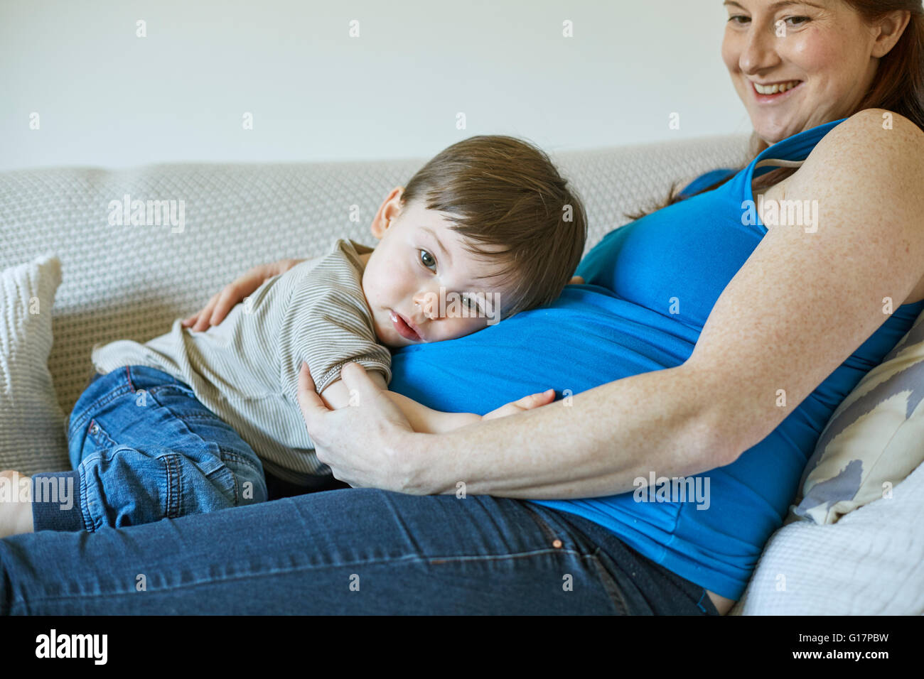 Baby Junge liegt auf Mütter schwanger Bauch Blick in die Kamera Stockfoto