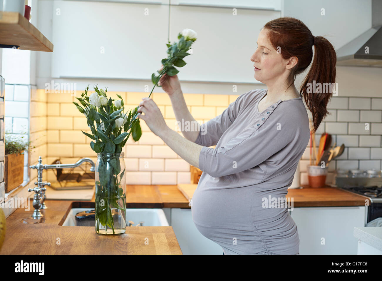 Seitenansicht der schwangeren Frau in der Küche, die Vermittlung von Blumen in vase Stockfoto