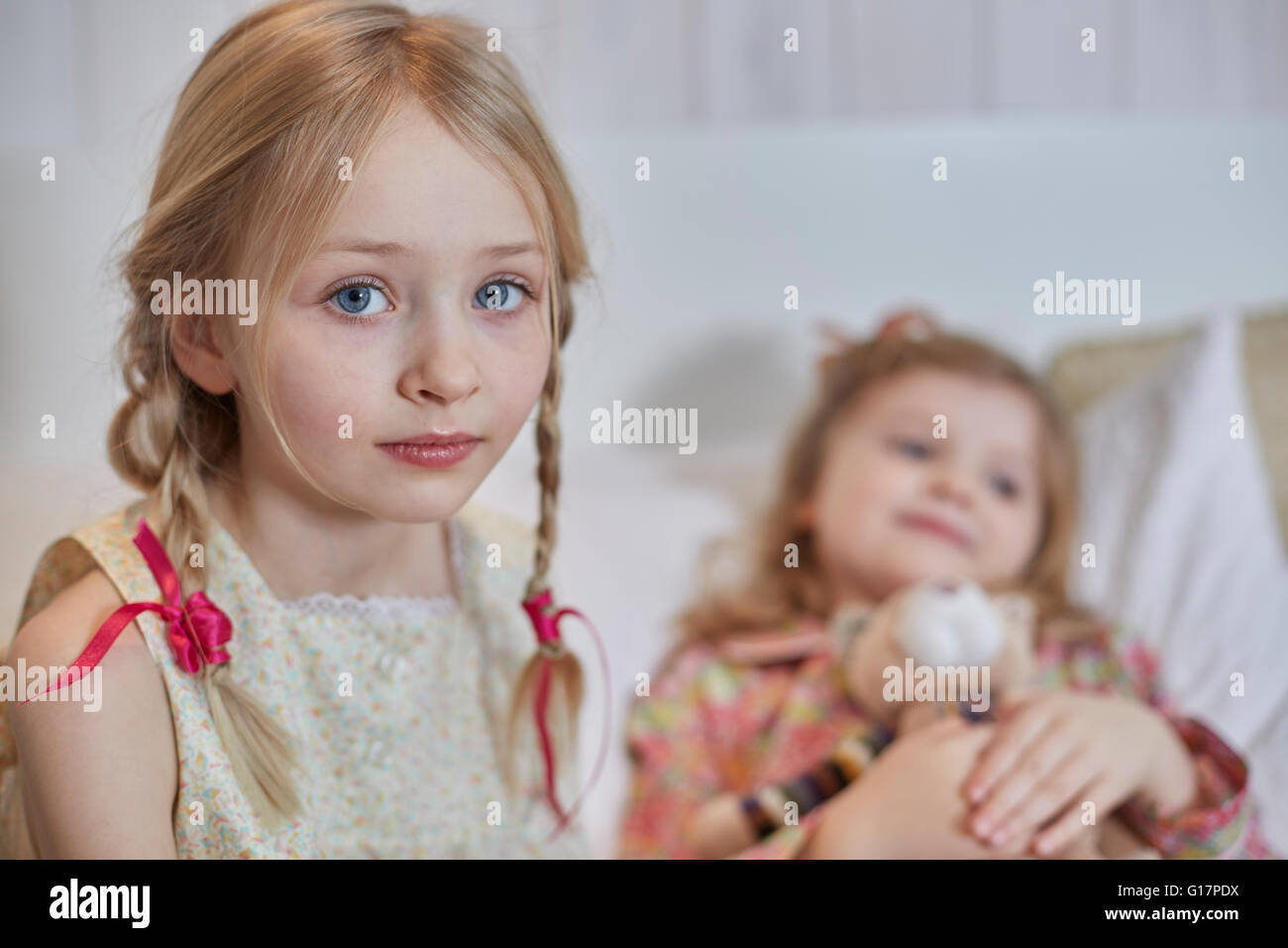 Mädchen mit geflochtenen Haaren, Schwester umarmt Teddybär im Hintergrund Stockfoto