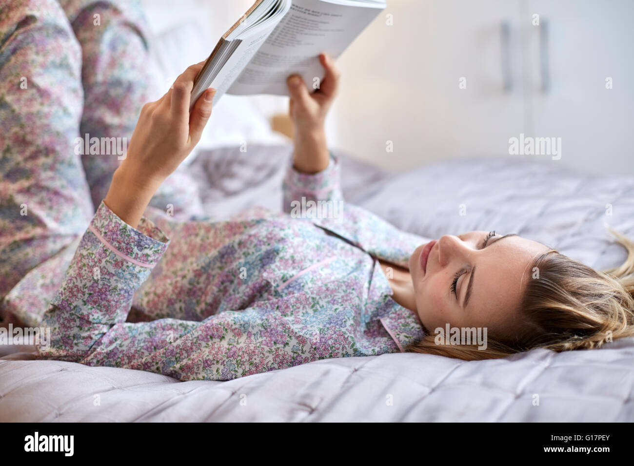 Frau im Schlafanzug Buch im Bett lesen Stockfoto