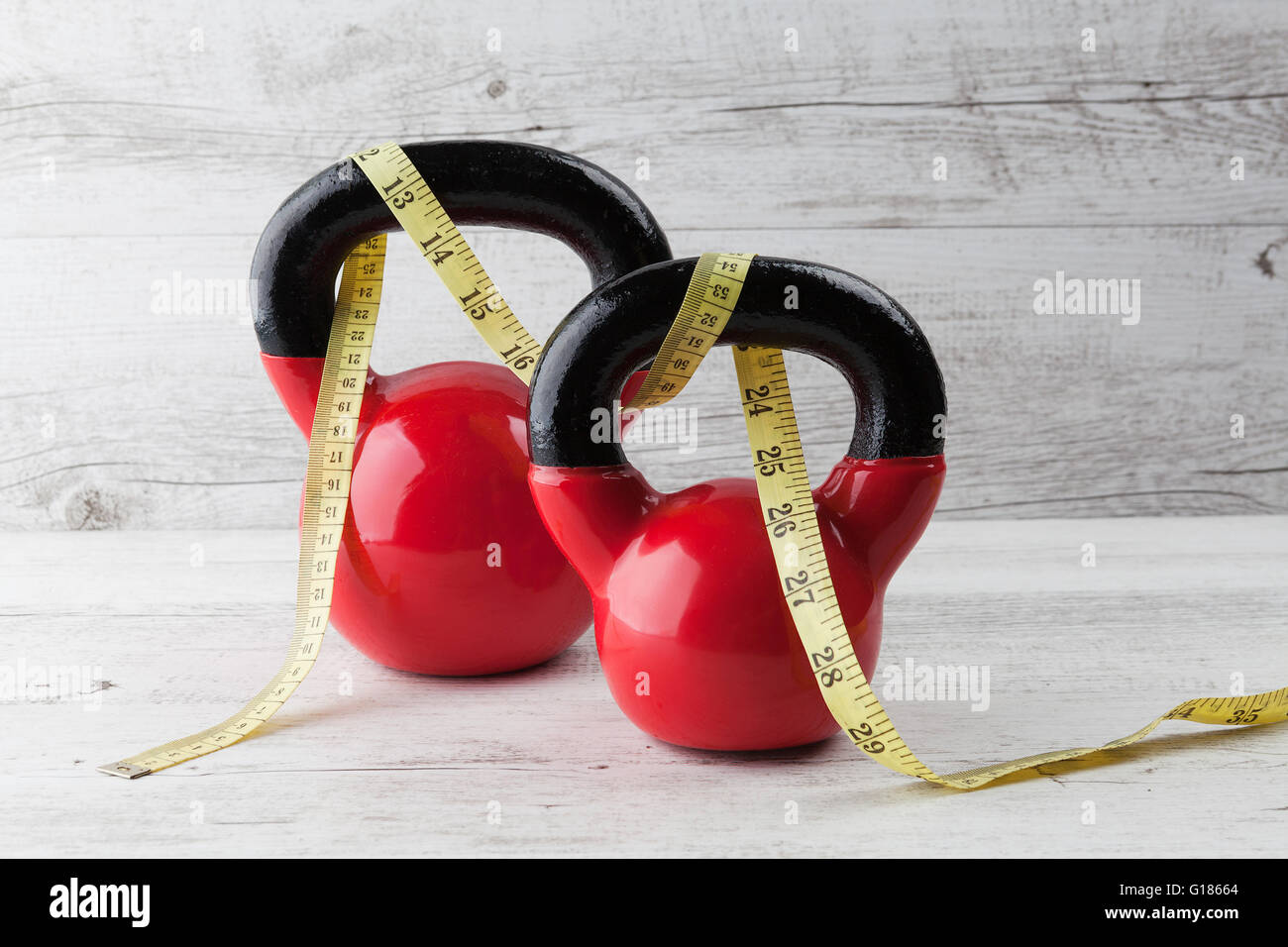 Zwei rote Kettlebells mit Maßband auf rustikalen weißer Holztisch. Gesundheit und Fitness-Konzept. Stockfoto