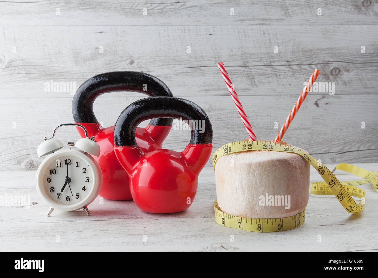 Zwei rote Kettlebells mit Maßband, Kokosnuss, Strohhalme und Vintage Uhr auf rustikalen weißer Holztisch zu trinken. Gesunde Ernährung Stockfoto