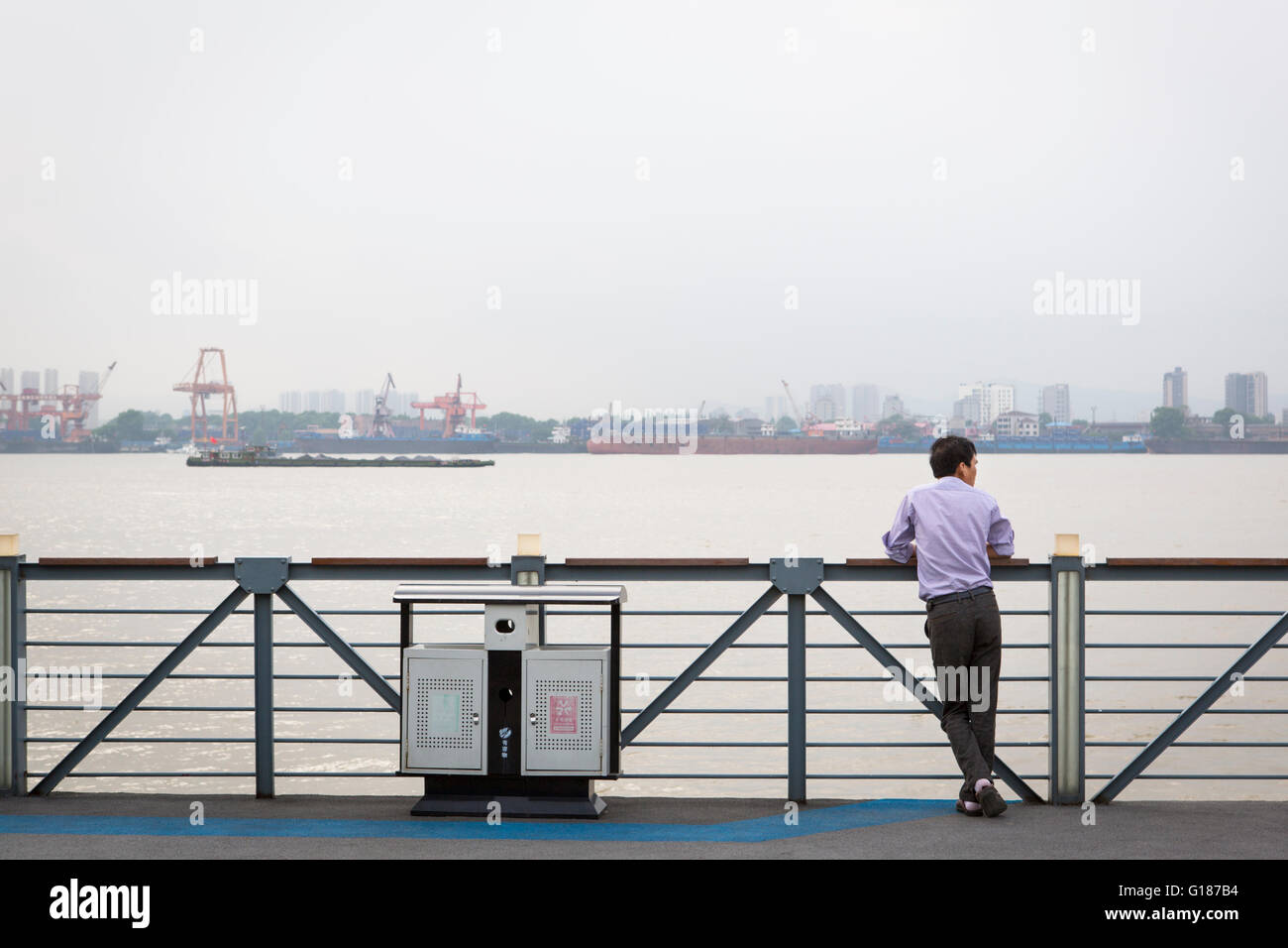 Chinesischer Mann betrachten am Jangtse-Fluss mit einem Schiff und Werften in Nanjing / China Stockfoto