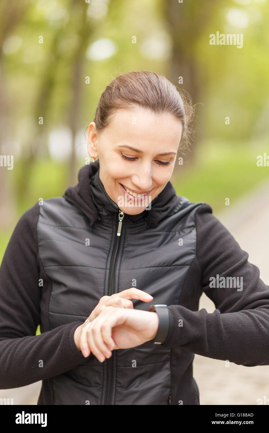 Junge Frau mit smart-Uhr nach dem Joggen für Herzfrequenzsteuerung. Lächelndes Mädchen mit Fitness Tracker Armband draussen zu Stockfoto