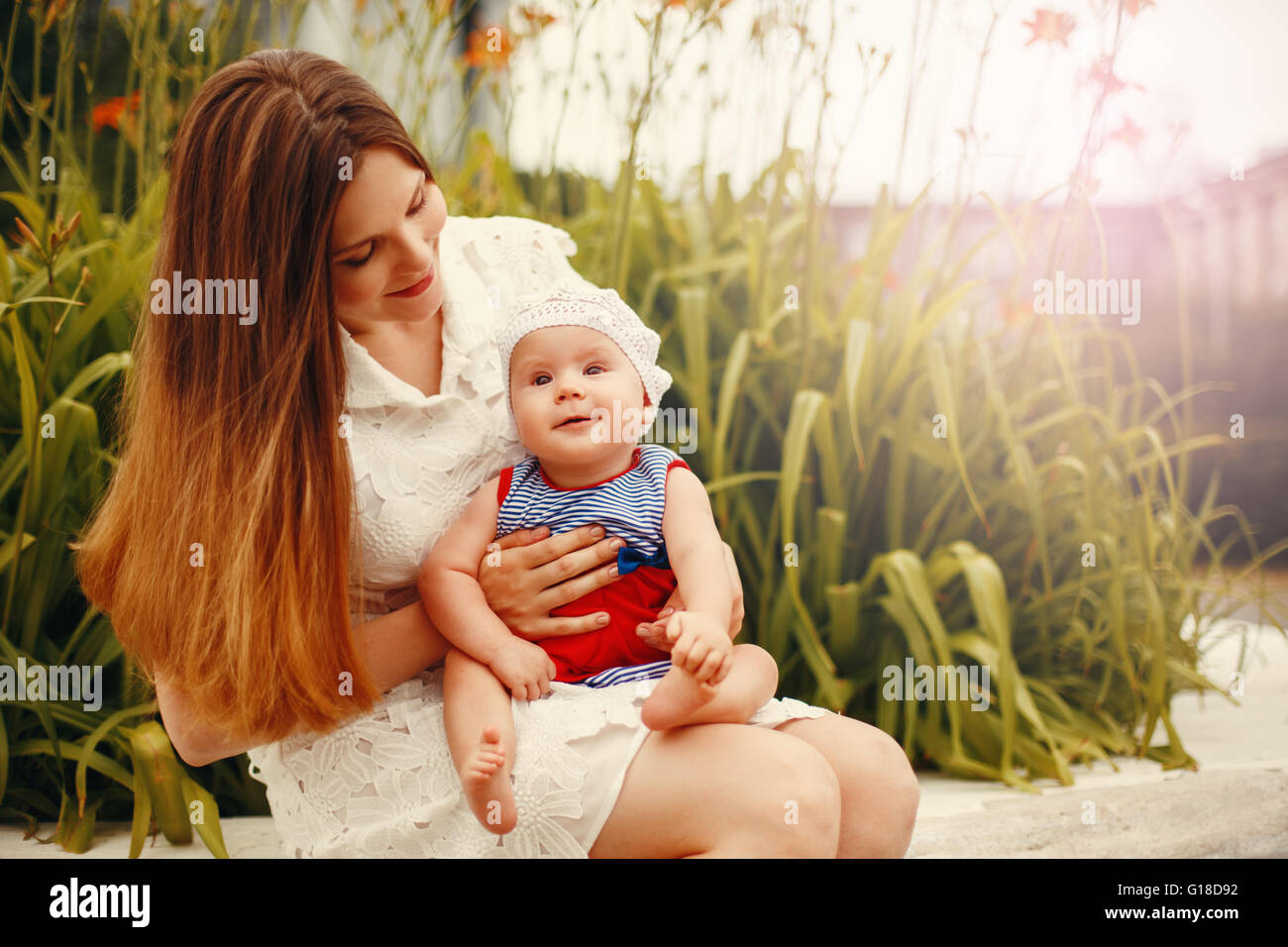 Niedliche glücklich Kleinkind auf liebevolle Mutter Knien sitzen und Lächeln auf den Lippen. Familienspaß. Bild mit warmen Farben abgeschwächt. Stockfoto