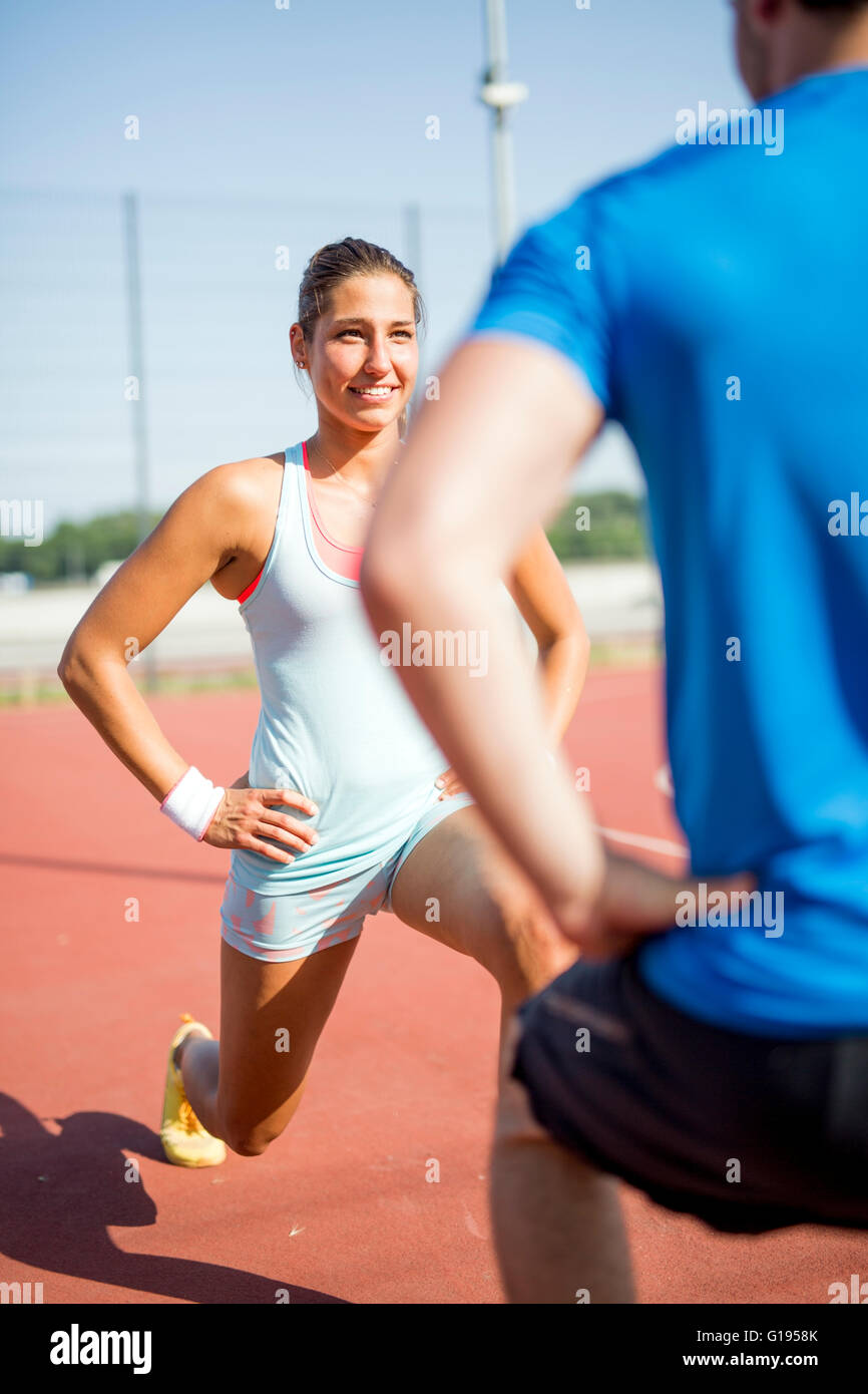 Junger sportlicher Mann und Frau dehnen im Freien an einem heißen Sommertag einander zugewandt Stockfoto