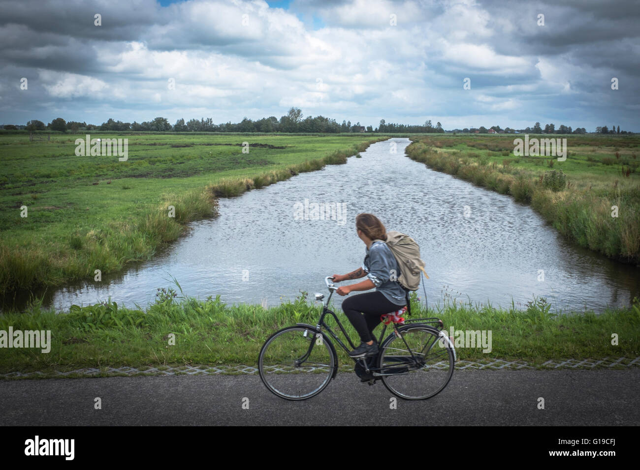 Frau auf einem Fahrrad fahren, vorbei an einem Fluss in den Niederlanden Stockfoto