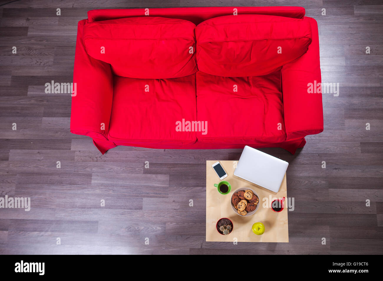 Rotes Sofa und Tisch mit Laptop, Handy, Tassen Kaffee und Gebäck Stockfoto