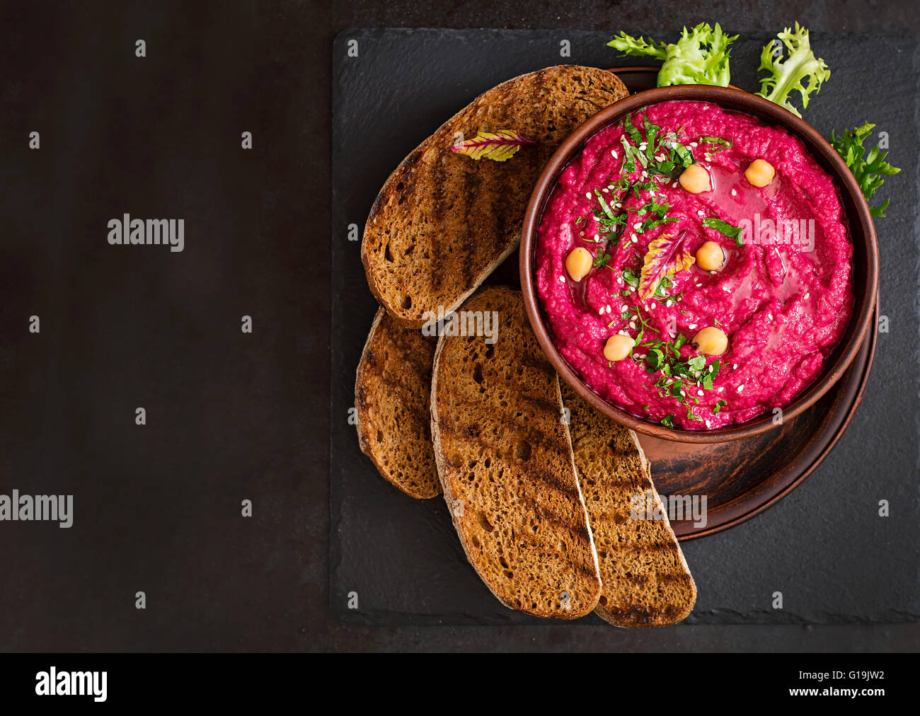 Geröstete Rüben Hummus mit Toast in einer Keramikschale auf einem dunklen Hintergrund. Ansicht von oben Stockfoto