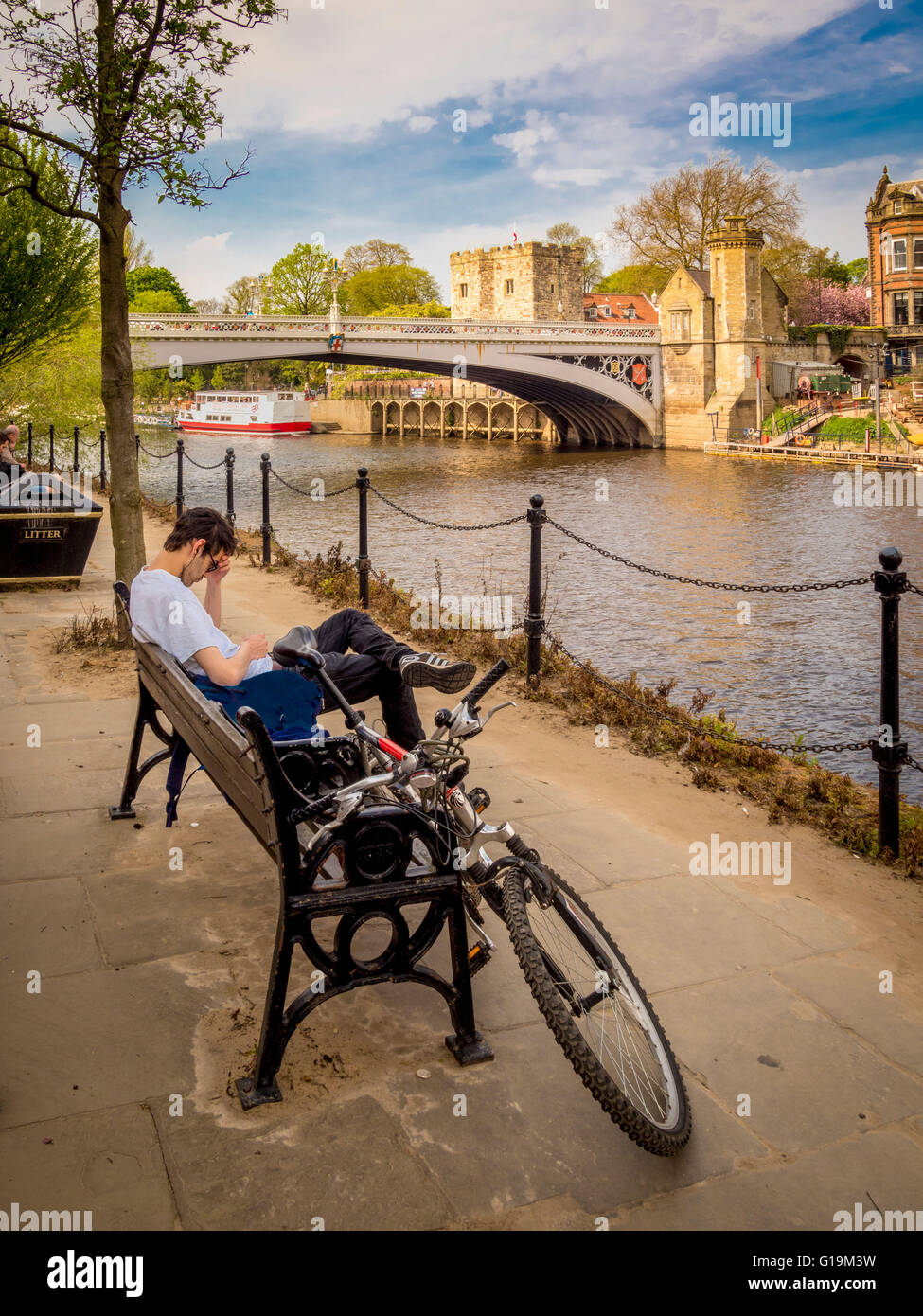 Radfahrer auf Bank überprüft Telefon mit Lendal Bridge im Hintergrund, York, UK. Stockfoto